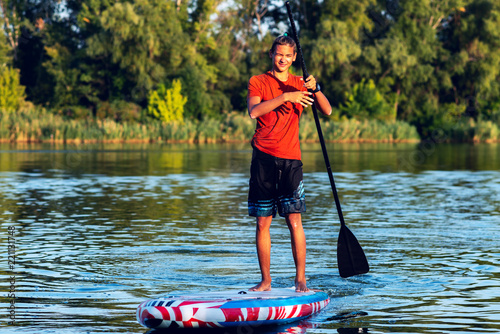 Happy guy, teenager paddling on a SUP board on large river