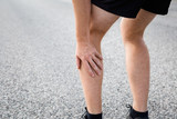 Man touching his leg during running time on asphalt road. Painful muscle, sprain or cramp ache. Sport problem and solution.