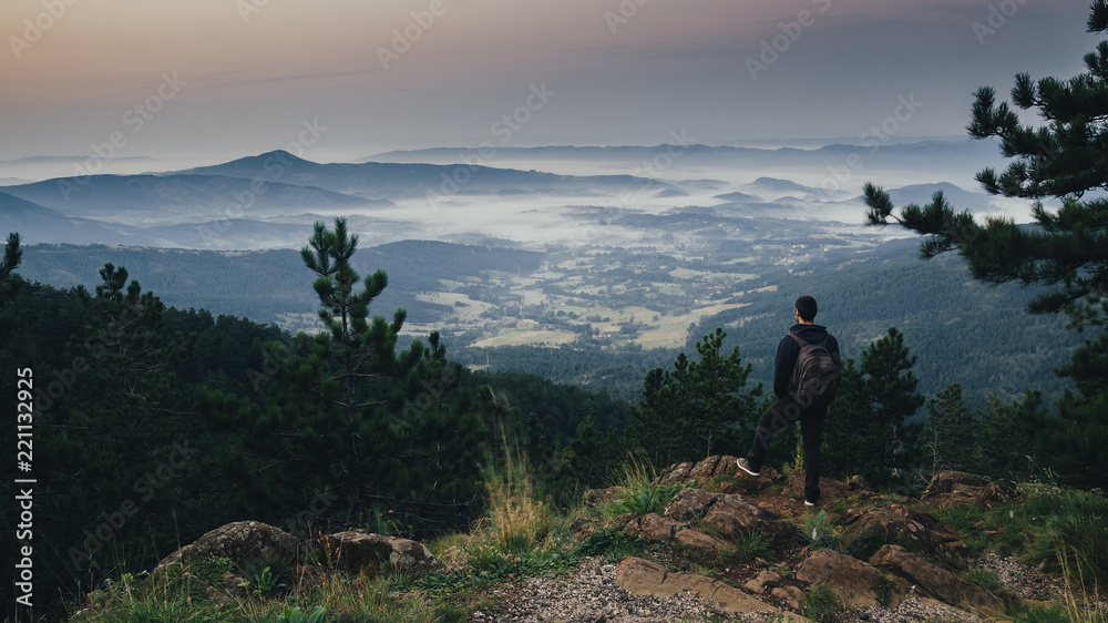 Hiker enjoying in the view on the valley and hills in the mist at sunrise