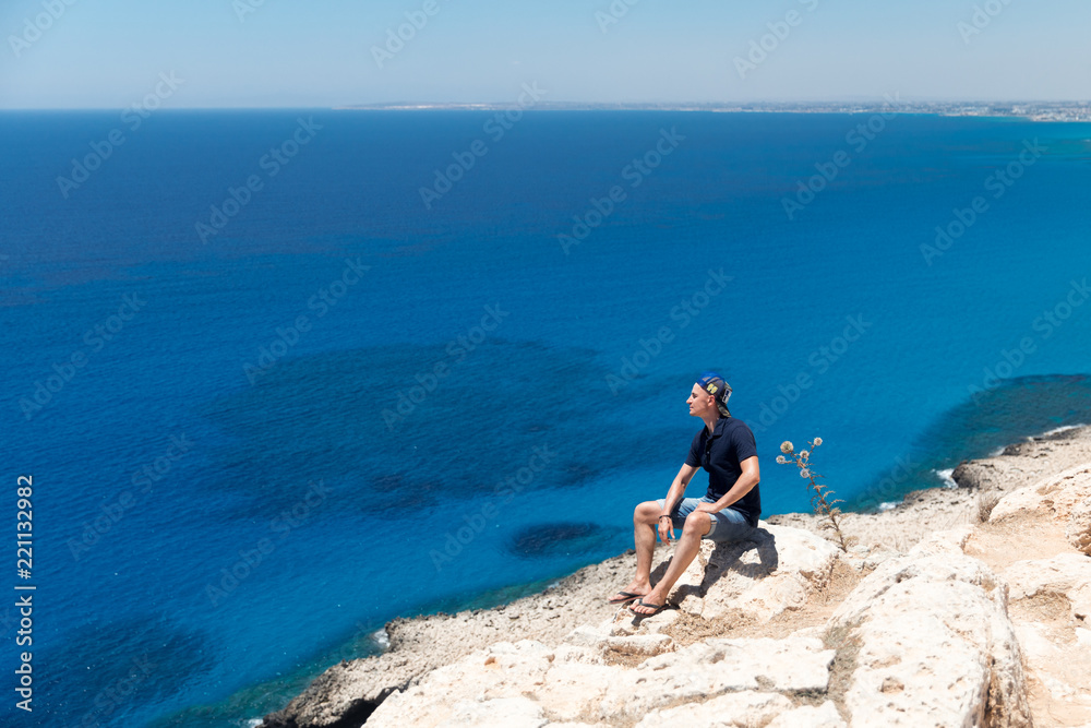 Bald man in a T-shirt and shorts sitting alone on top of a mountain overlooking the sea