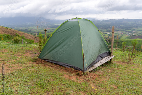 A small green tourist tent on grassy valley on mountain.