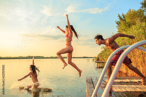 Group of friends jumping into the lake from wooden pier.Having fun on summer day.