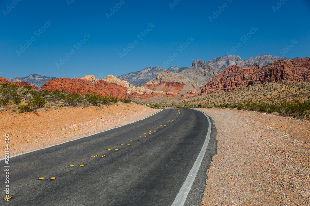 Paved Desert Road to Nowhere with Red Rock Mountains in the Distance with Blue Sky and Red Dirt in Nevada Paved Desert Road to Nowhere with Red Rock Mountains in the Distance with Blue Sky and Red Dirt in Nevada