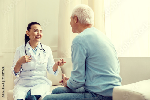 Regular checkup. Selective focus on a smiling lady gesturing while talking to a retired gentleman during a medical consultation.