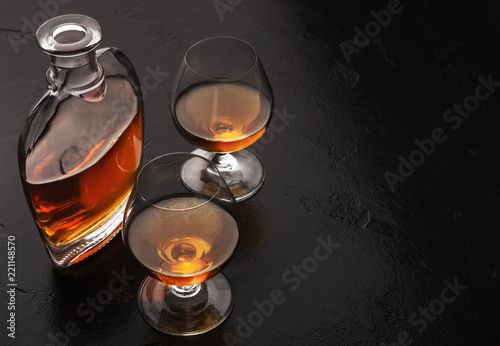 Two glasses of brandy or cognac and bottle on black