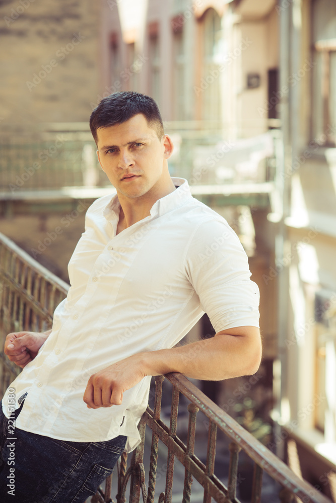 Fashion man relax on house balcony. Fashion model in fashionable shirt and jeans Fashion man relax on house balcony. Fashion model in fashionable shirt and jeans