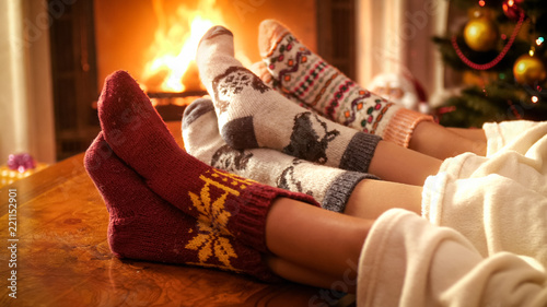 Closeup image of couple with child wearing knitted socks relaxing by the fire at house