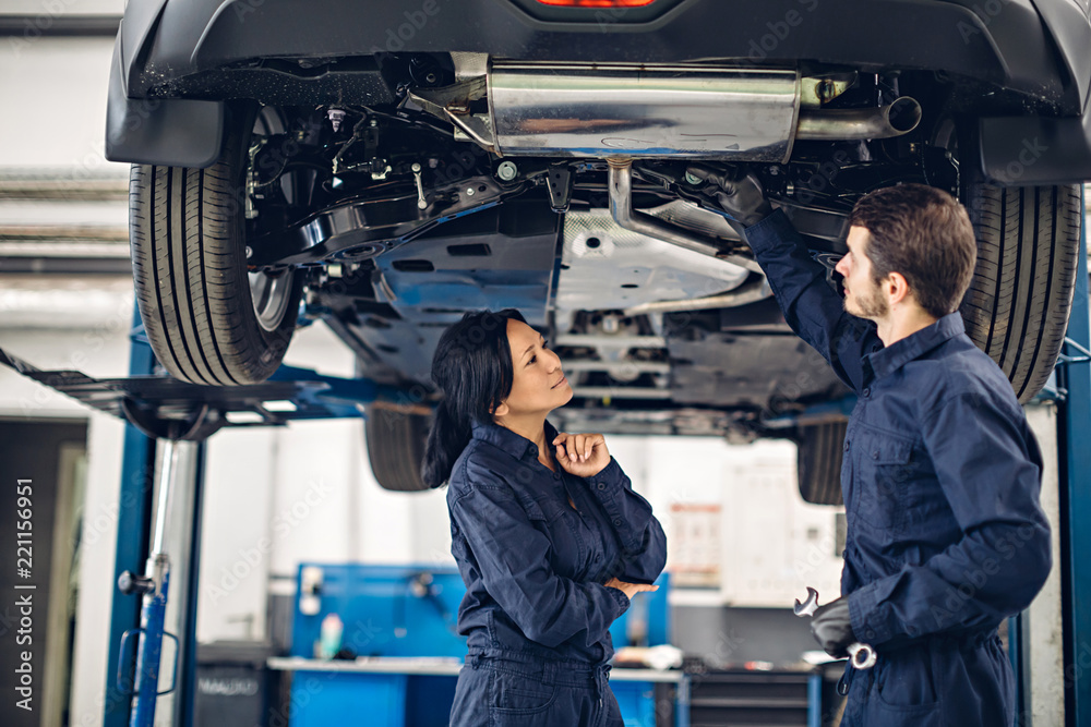 Auto car repair service center. Two mechanics - man and woman examining car