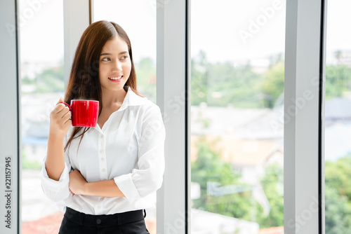Asian teenage Womanl Standing holding a red coffee glass standing by the window in the atmosphere during the morning work. Feel fresh, clear brain. Make it work full performance. Free Download Asian teenage Womanl Standing holding a red coffee glass standing by the window in the atmosphere during the morning work. Feel fresh, clear brain. Make it work full performance. - GFXLoad