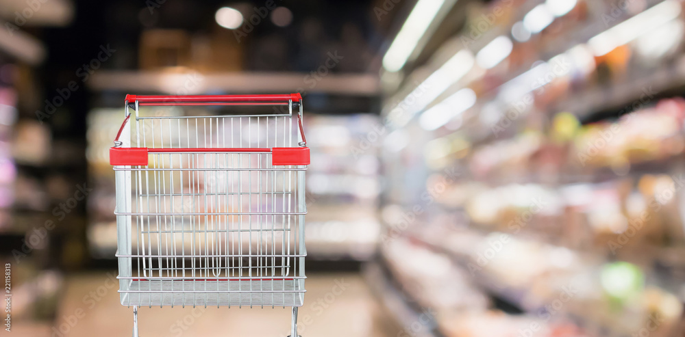 Empty red shopping cart with abstract blur supermarket discount store aisle and product shelves interior defocused background