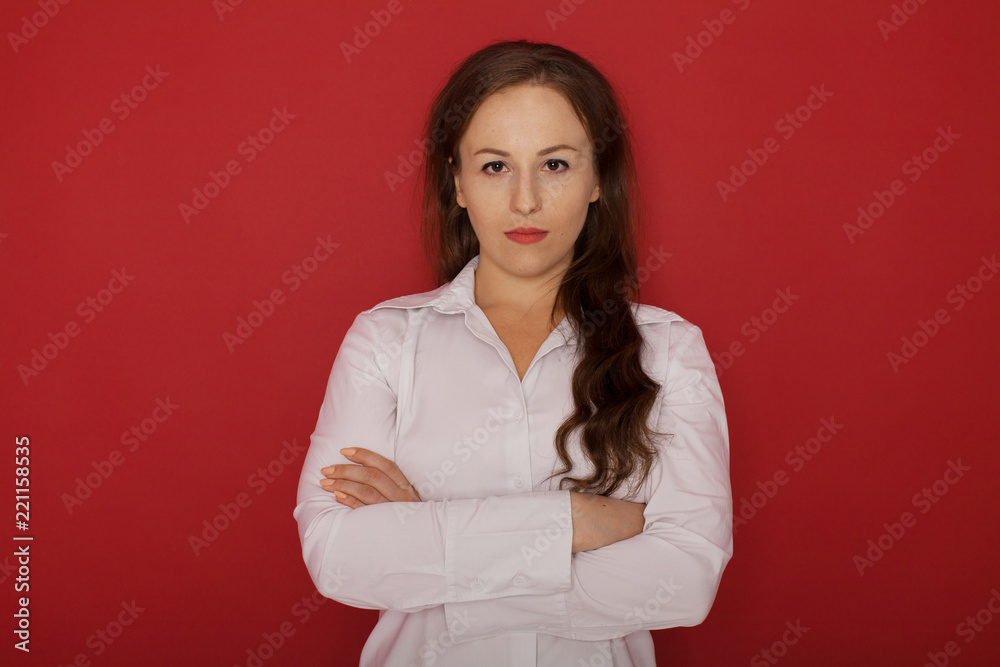 Charming businesswoman. Confident young businesswoman keeping arms crossed and looking at camera while standing against red background