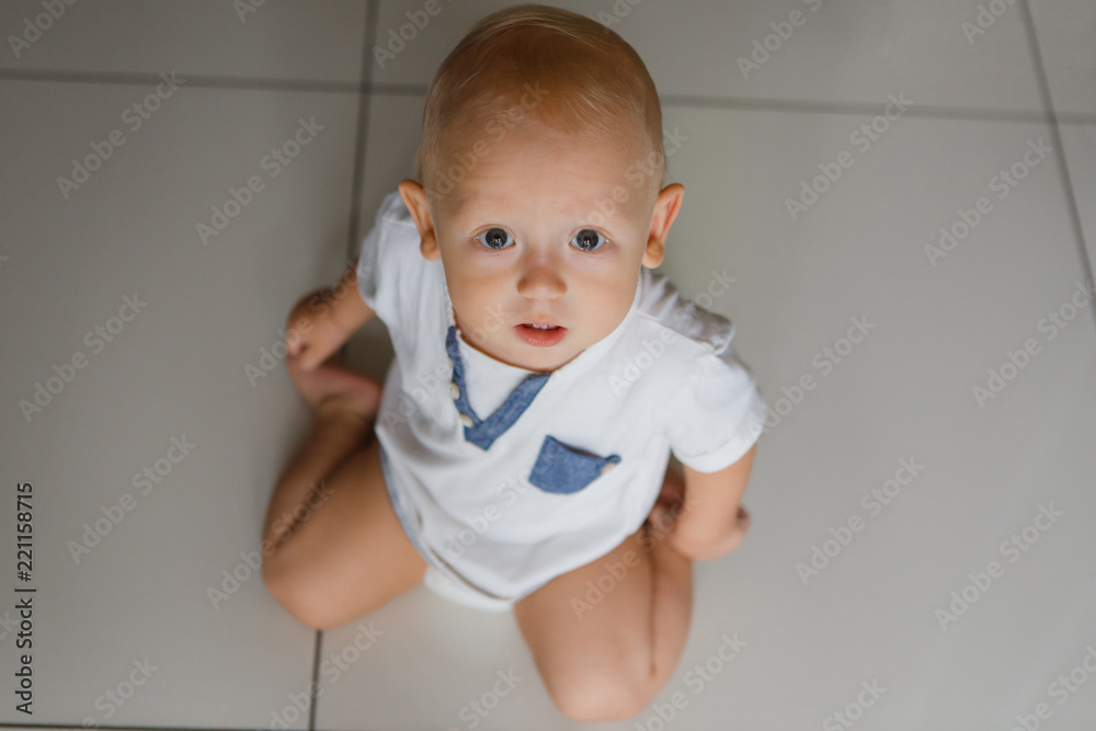 A 9 month old boy sits on the floor and looks up mournfully