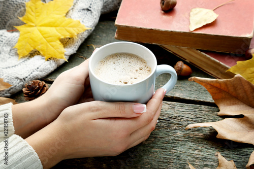 Female hands holding cup of coffee with dry leafs and books