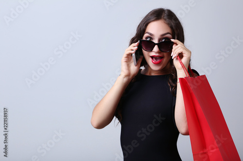 Happy woman with red shopping bag and smartphone on grey background