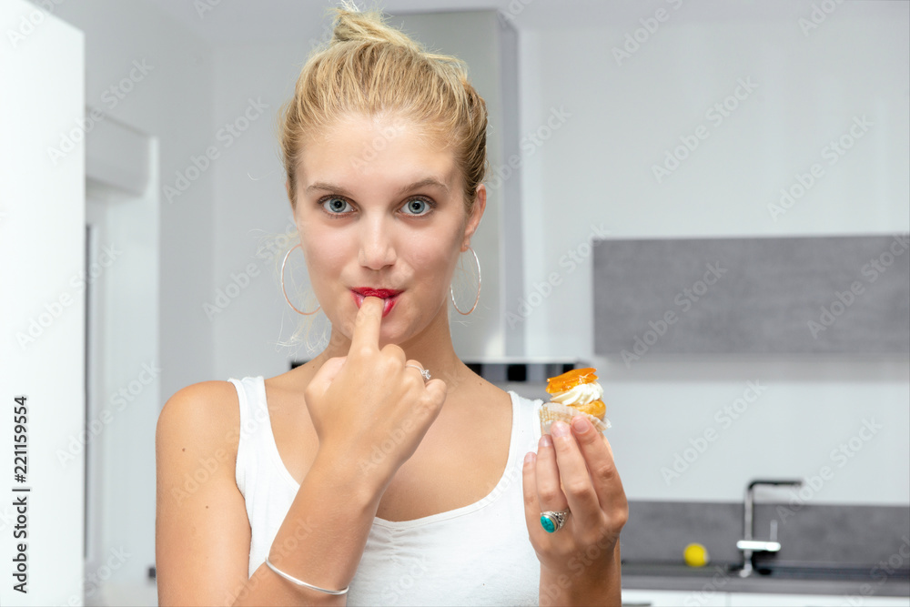 beautiful young blond woman eating cakes in the kitchen beautiful young blond woman eating cakes in the kitchen