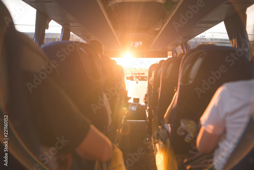 Background, bus interior. The salon of the bus with people fill the sun with light in the sunset. People travel on a big tourist bus. The bus rides along the mornings in the sunrise