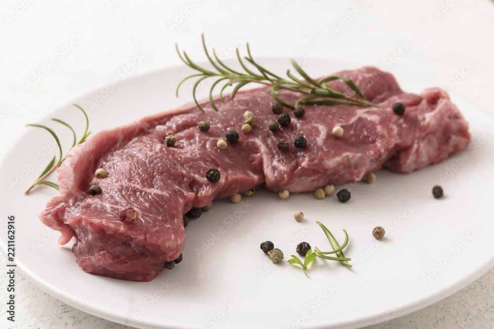 raw entrecote steak with rosemary and spices on a white plate