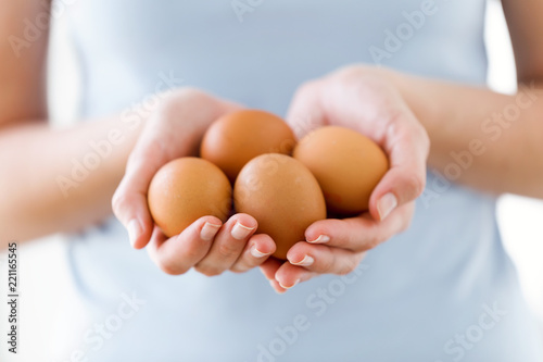 Young woman holding brown chiken eggs over white background.