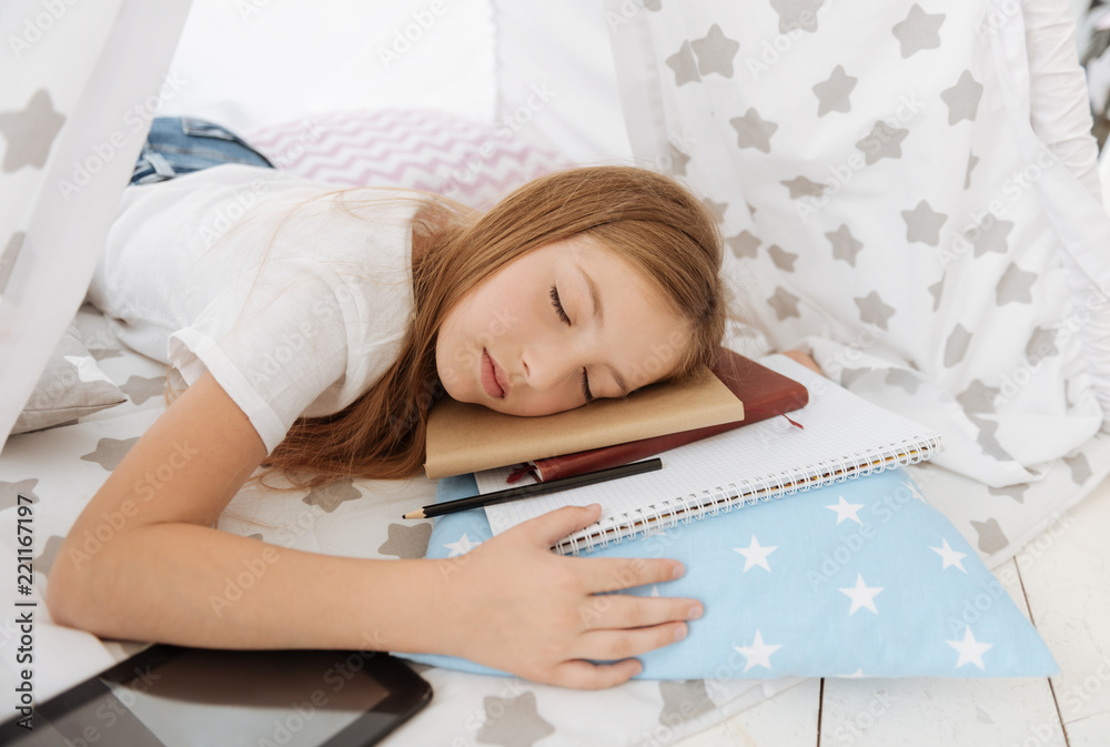 Fed up. Exhausted teenager keeping head on the books and closing eyes while having rest Fed up. Exhausted teenager keeping head on the books and closing eyes while having rest