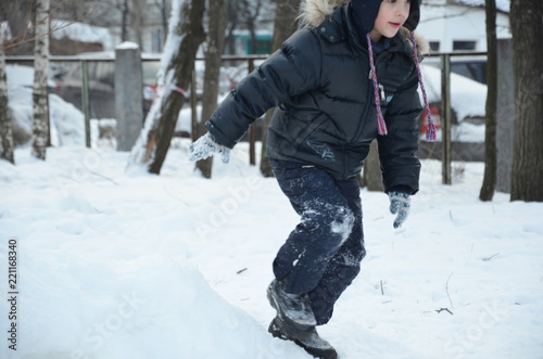 Baby boy walking at snowfall. Child in winter clothes playing with snow
