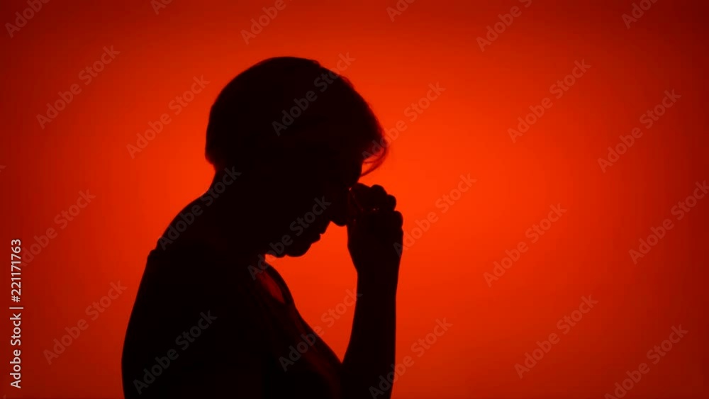 Silhouette of senior woman with eyeglasses. Female's face in profile putting on glasses on red background. Black contour shadow of grandmother's half-face holding spectacles Silhouette of senior woman with eyeglasses. Female's face in profile putting on glasses on red background. Black contour shadow of grandmother's half-face holding spectacles