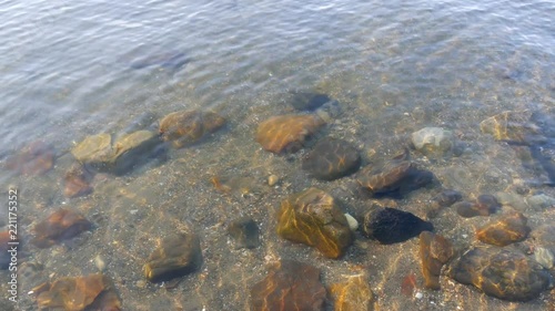 Video of several rocks and gravel on the bottom of the ocean at low tied with small waves shimmering above. photo