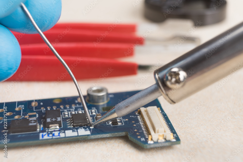 Fototapeta premium The hand holding the tin, a soldering iron solder the chip in place. Computer repair. Macrophotography.