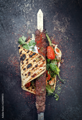 Traditional Adana kebap on a skewer with tomato and yogurt on a flatbread