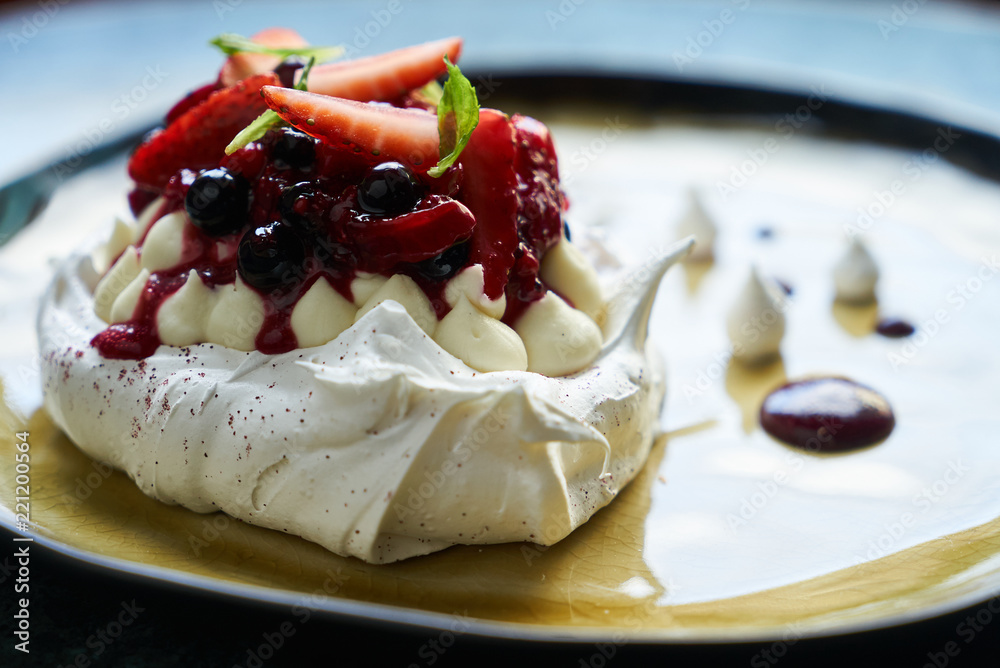 Pavlova meringue cake with fresh berries and custard cream on plate on green marble table background, close-up 