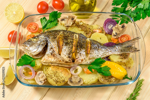 Baked sea bream with lemon, onions, herbs, cherry tomatoes, spices and baked potatoes on a wooden background. Fried tasty fish. Diet and healthy food.