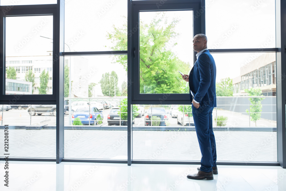 Black American Businessman Standing at the window, Calling Someone Through Mobile Phone.