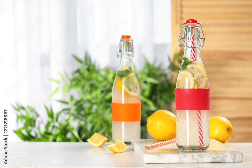 Bottles with natural lemonade on table against blurred background