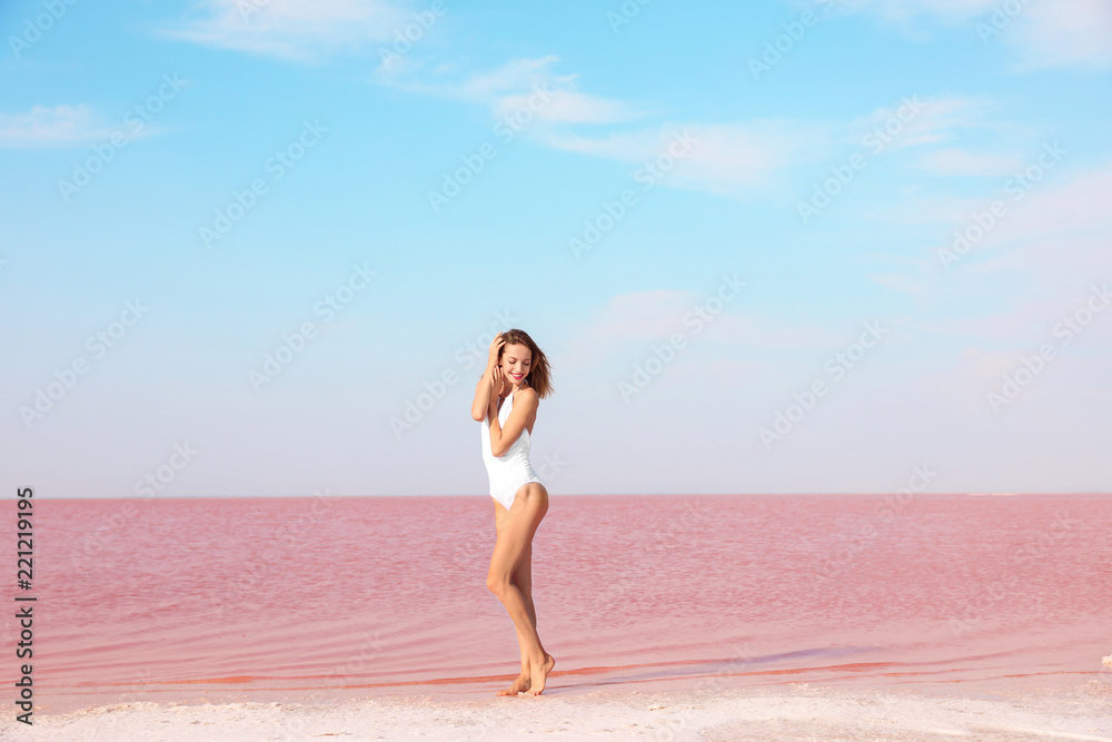 Beautiful woman in swimsuit posing near pink lake on sunny day Beautiful woman in swimsuit posing near pink lake on sunny day