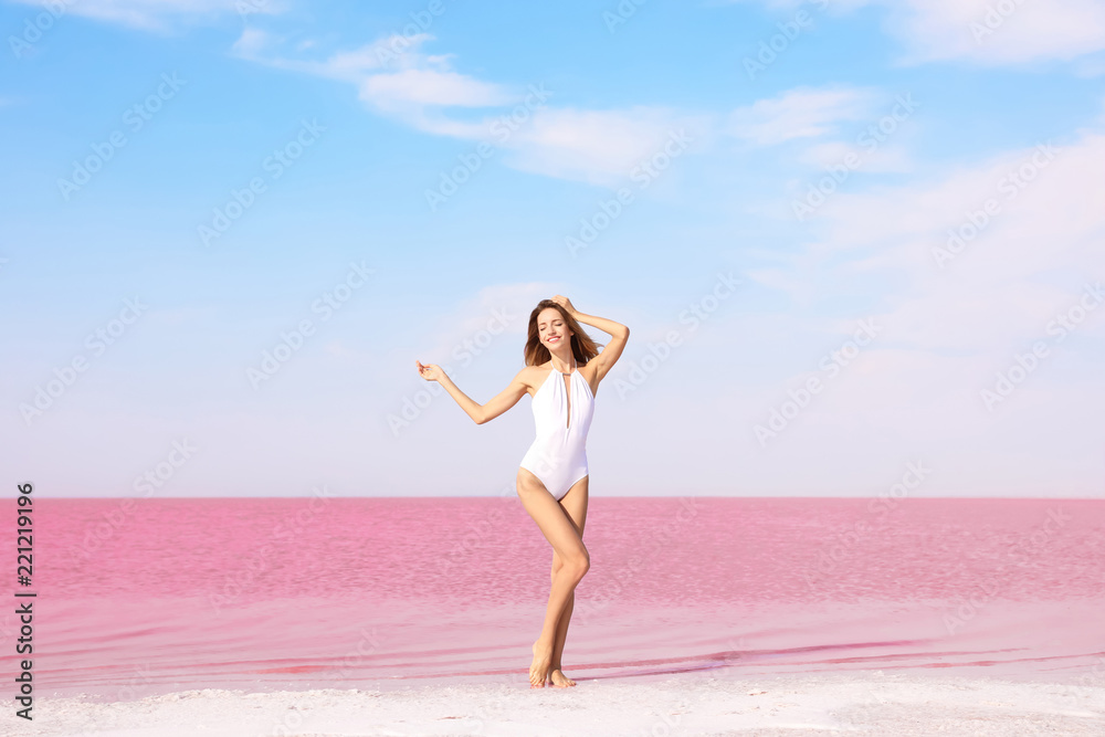 Beautiful woman in swimsuit posing near pink lake on sunny day