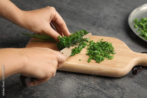 Woman cutting fresh green parsley on wooden board, closeup