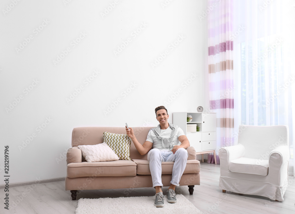 Happy young man operating air conditioner with remote control at home