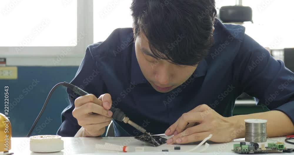 Asian electronics engineer is soldering an electric board in his workshop. Asian student are studying electronics and soldering in classroom.
