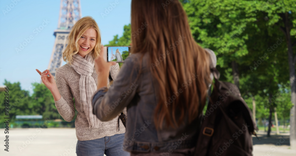 Fototapeta premium Charming young woman taking picture of friend standing in front of Eiffel Tower