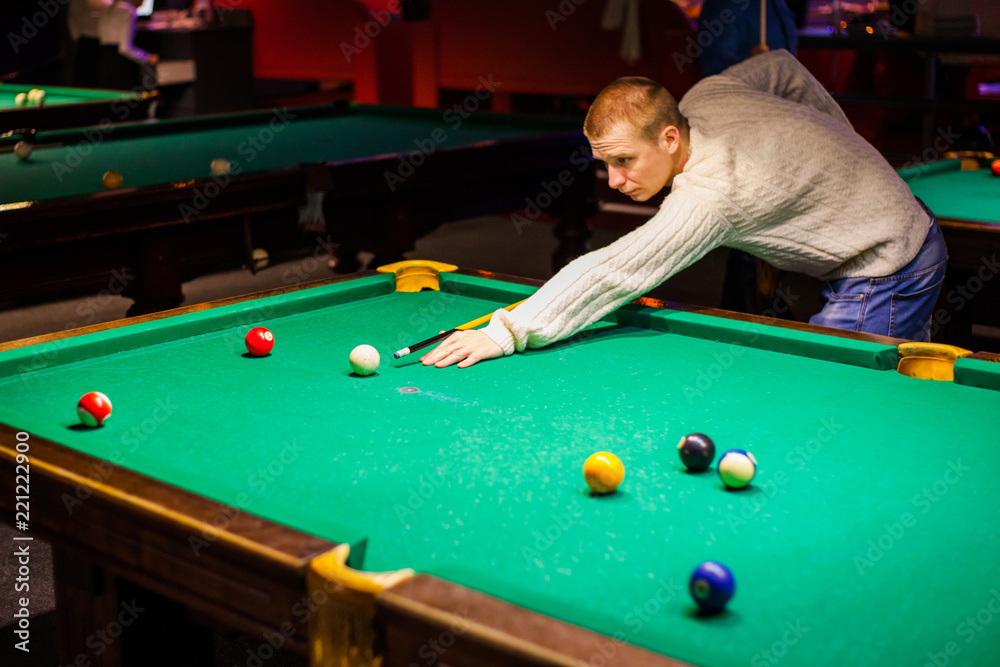 Fototapeta premium young handsome guy in a white sweater playing billiards