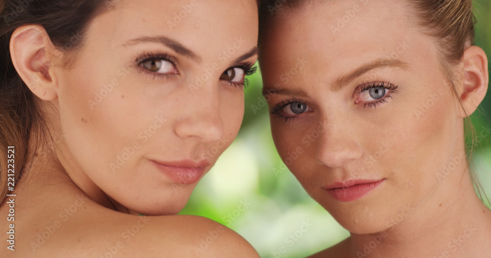 Closeup of pair of white women staring intimately on green and white background