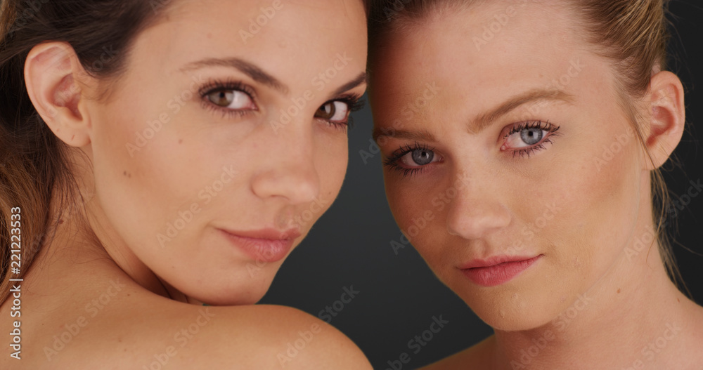 Close view of blonde and brunette staring at camera on solid gray background Close view of blonde and brunette staring at camera on solid gray background