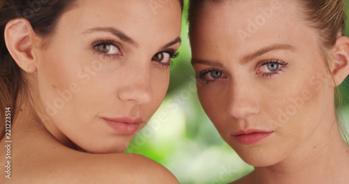 Closeup of pair of white women staring intimately on green and white background