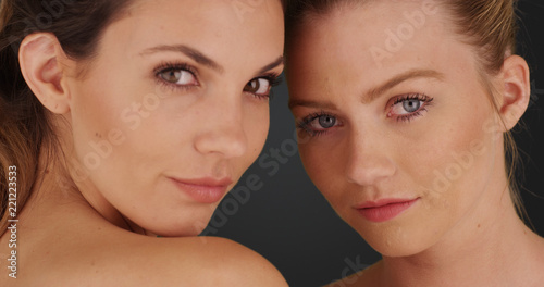 Close view of blonde and brunette staring at camera on solid gray background