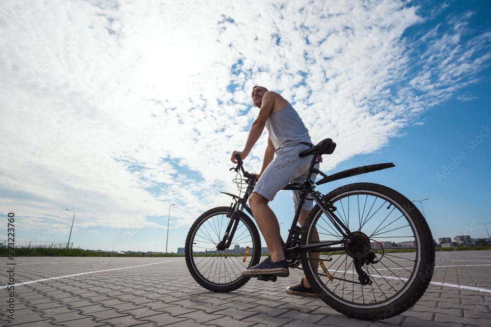 Obraz premium beautiful young guy with a bicycle against the sky on a sunny day