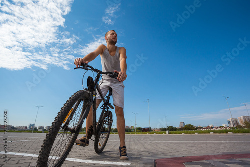 beautiful young guy with a bicycle against the sky on a sunny day