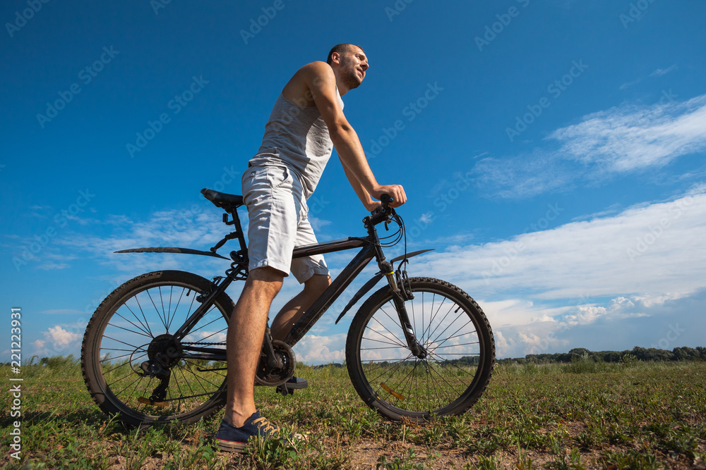 beautiful young guy with a bicycle against the sky on a sunny day