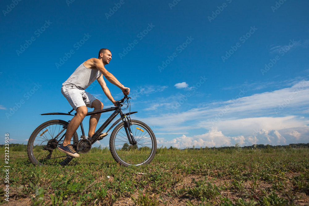 beautiful young guy with a bicycle against the sky on a sunny day