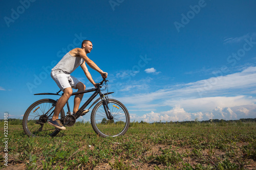 beautiful young guy with a bicycle against the sky on a sunny day © Sergey