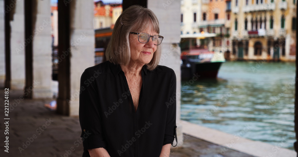 Somber senior lady thinking to herself seated outdoors while in Venice, Italy