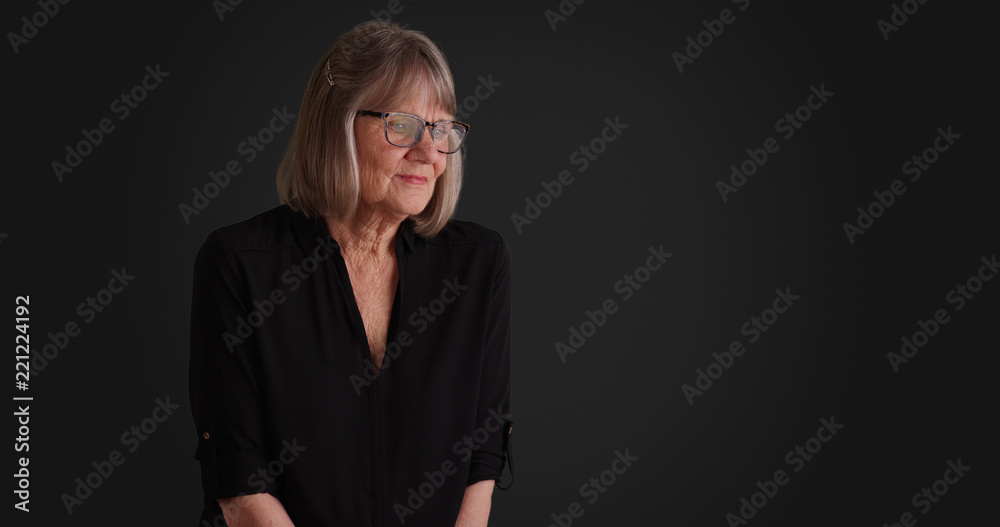 Somber senior lady thinking to herself seated alone on gray background Somber senior lady thinking to herself seated alone on gray background